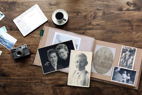 old photos in a photo album next to a camera, cup of coffee, and an ipad