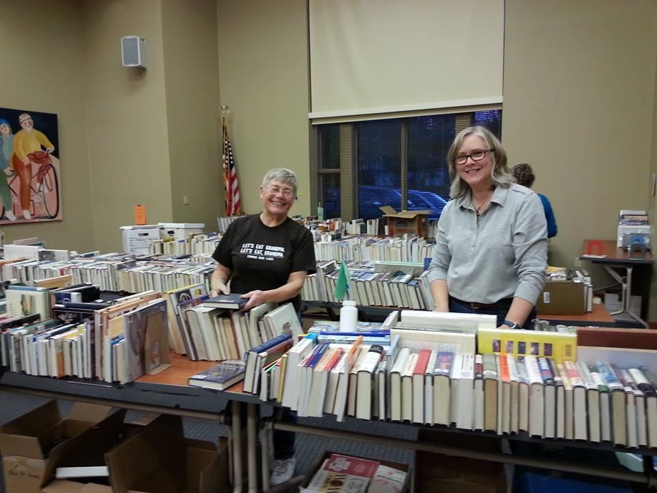 Two women standing behind tables filled with books.